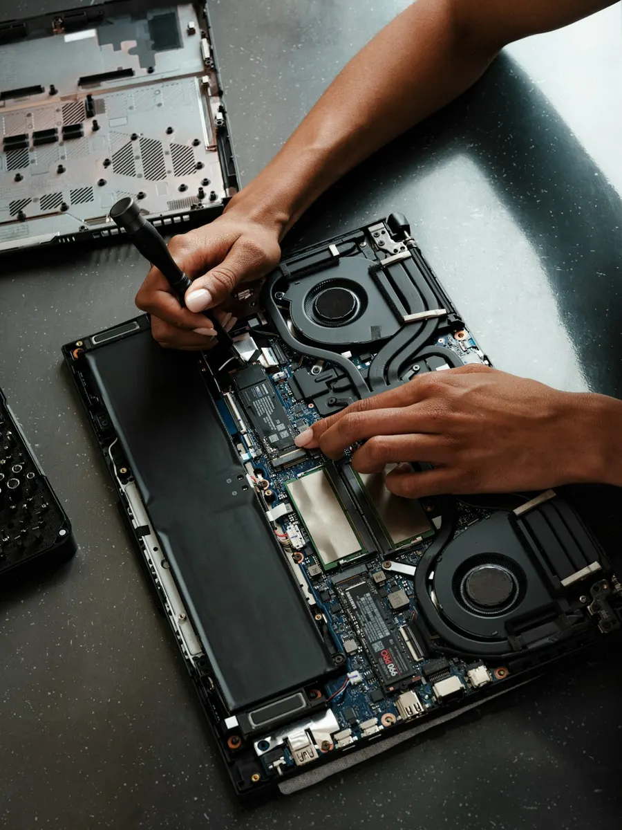 Técnico trocando peças de um notebook aberto na bancada, com ventoinhas, SSD, memórias e bateria à mostra